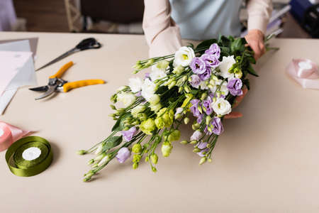 partial view of florist holding eustoma flowers near decorative tape, secateurs and scissors on...
