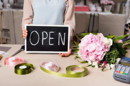 Cropped view of florist holding chalkboard with open lettering near bouquet on desk on blurred backgroundの写真素材