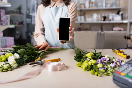 Cropped view of florist showing smartphone with blank screen with eustoma flowers on desk on blurred...