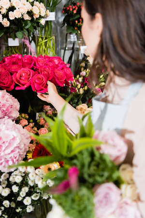Brunette florist touching rouses in vase on rack of flowers with blurred bouquet on foreground