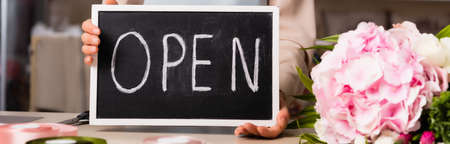 Cropped view of florist holding chalkboard with open lettering near blooming hydrangea on blurred background, bannerの写真素材