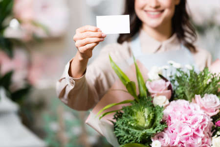 partial view of smiling florist holding blank business card and festive bouquet on blurred backgroundの写真素材
