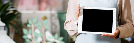 Cropped view of female florist holding digital tablet with blank screen on blurred background,...