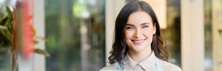 cheerful florist looking at camera near flower shop on blurred background, banner