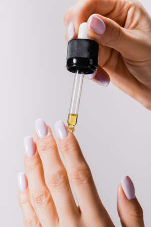 cropped view of woman applying oil from pipette on fingernails isolated on grayの写真素材
