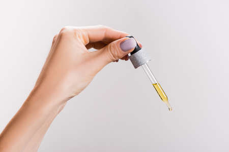 cropped view of woman holding pipette with oil isolated on grayの写真素材