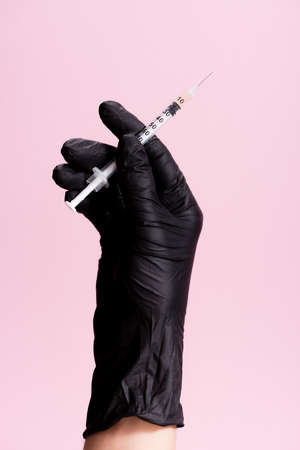 cropped view of hand in black latex glove with syringe isolated on pinkの写真素材