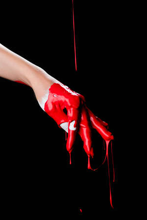 partial view of painted hand with red dripping paint isolated on black