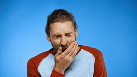 tired man yawning and covering mouth on blueの写真素材