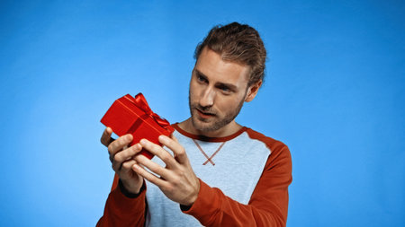 curious young man looking at wrapped red present on blueの写真素材