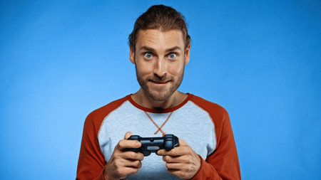 Excited man holding joystick while playing video game on blue