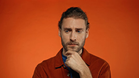 thoughtful man touching beard on orange background