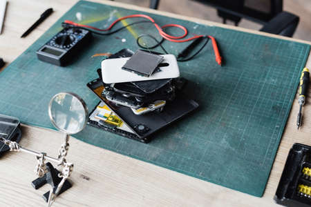 High angle view of pile of disassembled mobile phones on workplace with screwdriver, magnifier and...