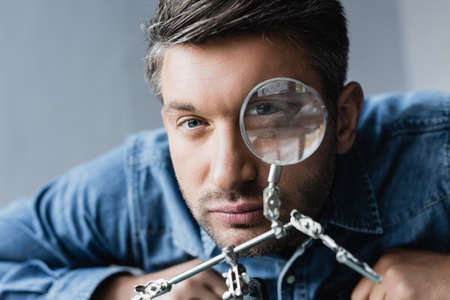 Portrait of repairman looking at camera through magnifier on blurred background