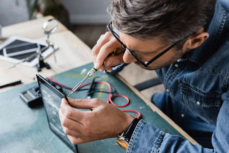 High angle view of repairman with screwdriver fixing smashed display of tablet at workplace on...