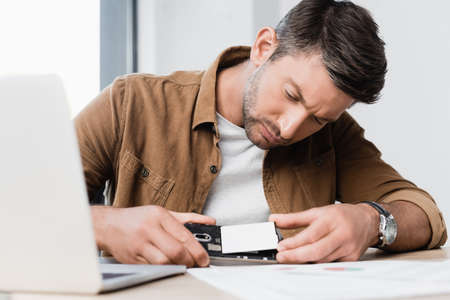Concentrated businessman putting battery in broken mobile phone at workplace on blurred foreground