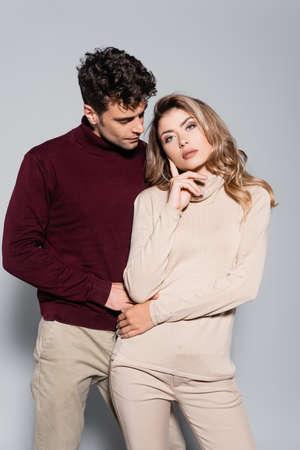 casual young couple in turtleneck jumpers posing isolated on grey background
