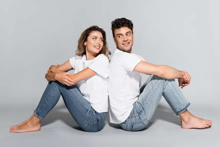 young couple in white t-shirts and jeans posing back to back isolated on grayの写真素材