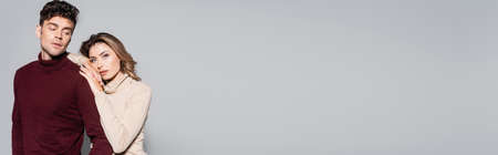 casual young couple in turtleneck jumpers embracing isolated on grey background.の写真素材