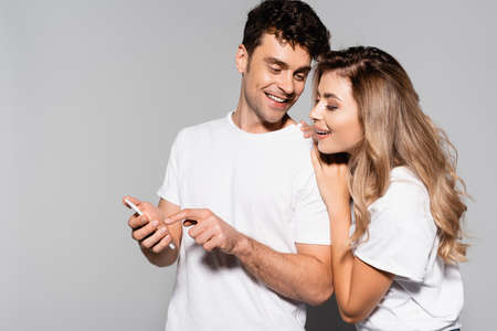 happy casual young couple in white t-shirts with smartphone isolated on grey backgroundの写真素材