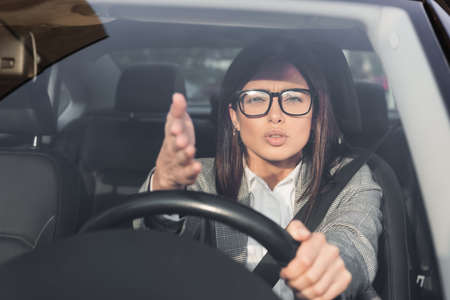 displeased woman looking at camera and pointing with hand while driving car on blurred foreground