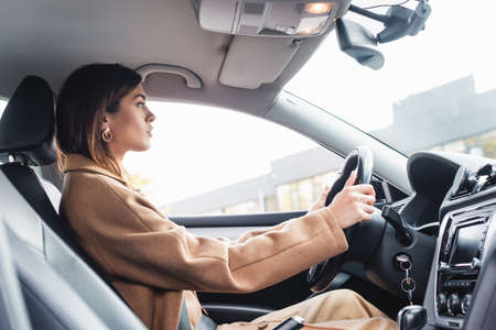 side view of woman in trench coat driving car on blurred foreground