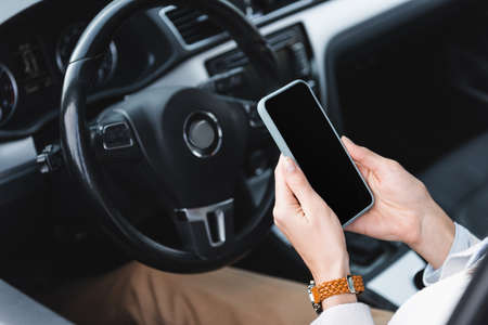 partial view of woman in wristwatch holding smartphone with blank screen near steering wheel on...
