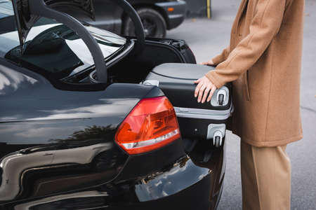 cropped view of woman in autumn clothes putting suitcase in car trunkの写真素材