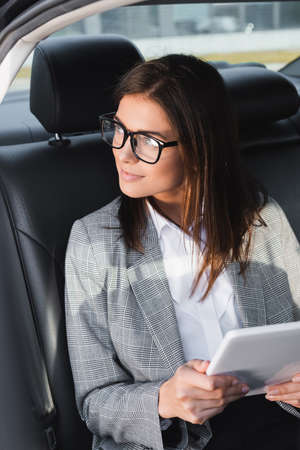 smiling businesswoman with digital tablet looking away while riding in car