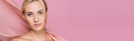 beautiful blonde woman with freckles and bare shoulders near curtain isolated on pink backgroundの写真素材