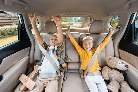 Smiling kids showing yes gesture while sitting near toys in auto