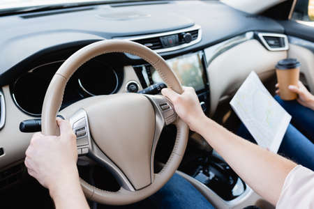 Cropped view of man driving car near wife with map and takeaway coffee on blurred backgroundの写真素材