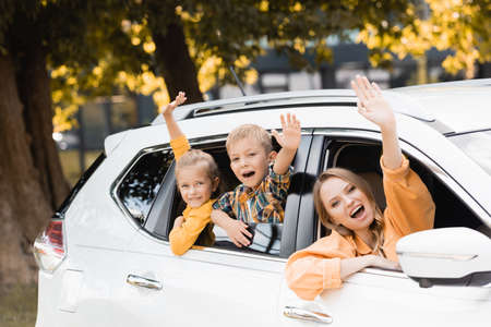 Smiling children waving hands near mother during travel in carの写真素材