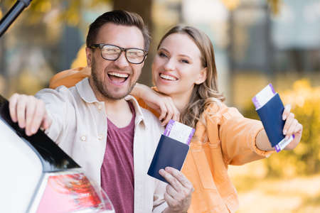 Cheerful woman embracing husband while holding passports with air tickets near carの写真素材
