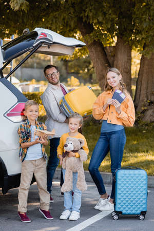 Cheerful family with passports and suitcases standing near auto outdoors