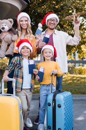 Cheerful family in santa hats holding passports near suitcases and car outdoorsの写真素材