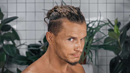 shirtless young man looking at camera with plants on blurred background