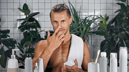 bearded man applying face cream in bathroom with plants on blurred backgroundの写真素材