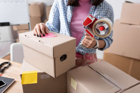 Cropped view of female volunteer holding scotch dispenser near carton boxes in charity center on blurred backgroundの写真素材