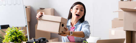 Excited asian volunteer with open mouth showing carton box in charity center, banner