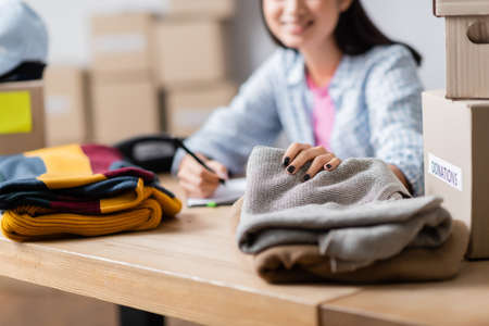 Cropped view of woman holding clothes near carton packages on blurred background on tableの写真素材