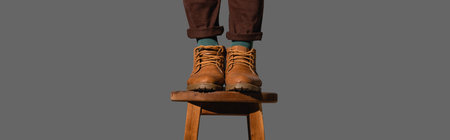 cropped view of man in boots standing on wooden chair isolated on gray, banner
