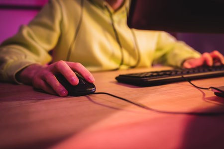 Cropped view of gamer using computer mouse near keyboard on blurred background