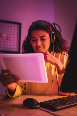 Smiling african american gamer in headset holding digital tablet on blurred foregroundの写真素材