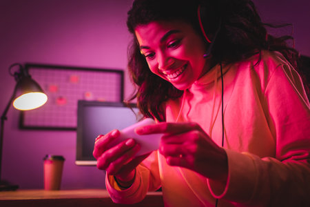 Smiling african american gamer in headset using smartphone on blurred foregroundの写真素材
