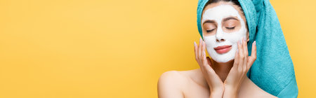 beautiful woman with closed eyes, blue towel on hair and clay mask on face isolated on yellow,...