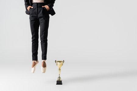 cropped view of african american businesswoman in pointe shoes jumping near golden cup on grayの写真素材