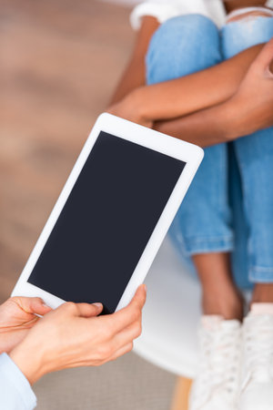 Cropped view of psychologist with digital tablet near blurred african american girl on backgroundの写真素材