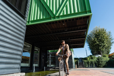 full length of businessman in wireless earphones riding bicycle and looking awayの写真素材