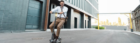 full length of businessman in formal wear riding modern electric scooter near building, bannerの写真素材